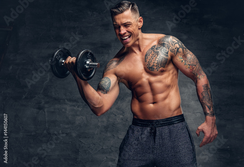 Athletic  male with tattoo on his chest doing biceps workouts with dumbbell. © Fxquadro