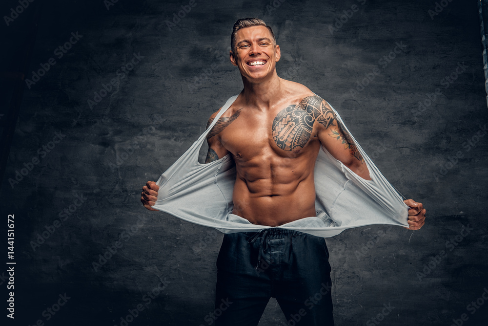 Smiling muscular male with tattooed torso ripping t shirt on his chest ...