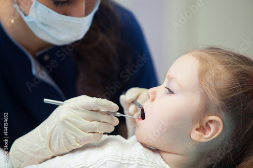 female dentist in mask treats teeth little girl