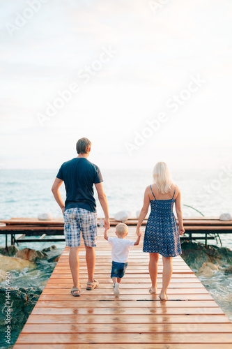 Parents with a daughter at the sea. Dad and mom are holding the baby by the hand.