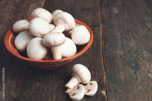 Fresh white mushrooms champignon in brown bowl on wooden background. Top view. Copy space.