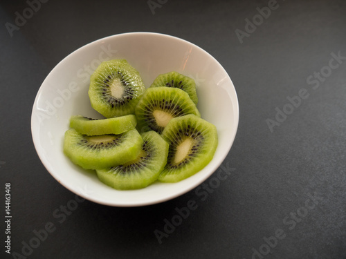 Slices of kiwi in a white plate on dark background. Selective focus with shallow depth of field.