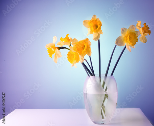 Fototapeta Naklejka Na Ścianę i Meble -  Narcissuses in a glass vase on a white table.