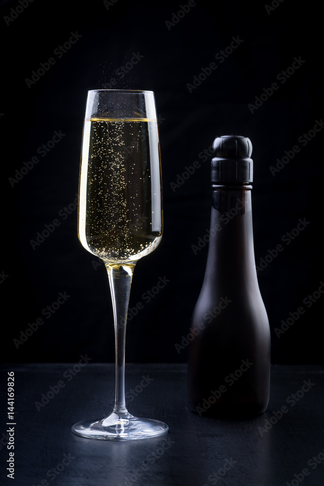 champagne sparkling white wine glass and bottle on black background with strawberry garnish gold ribbon