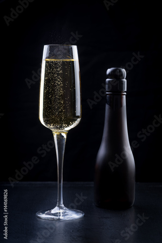 Obraz na płótnie champagne sparkling white wine glass and bottle on black background with strawberry garnish gold ribbon w salonie