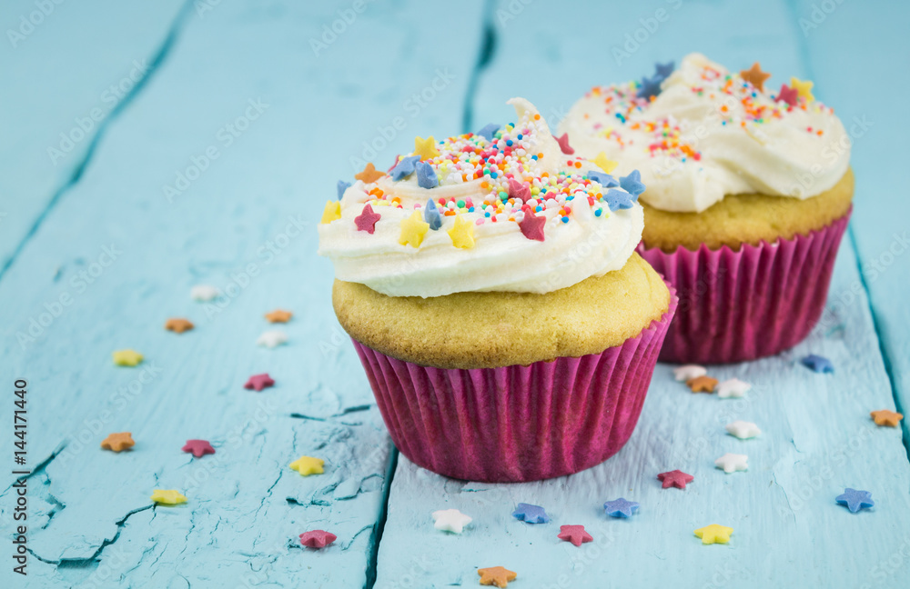 Two cup cakes with star sprinkles on blue table - background Two cup cakes with star sprinkles on blue table - background