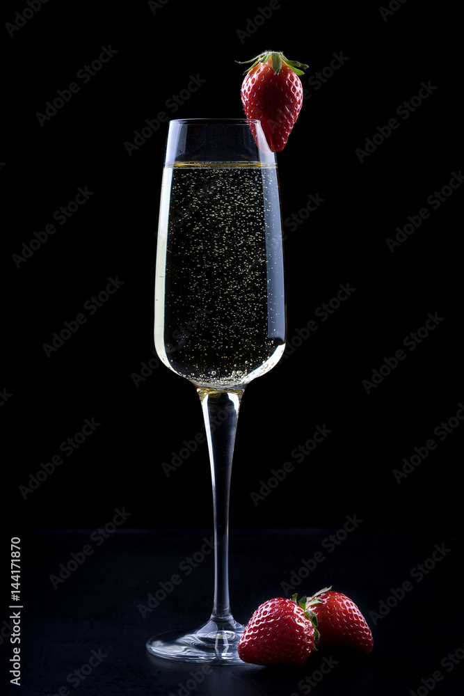 champagne sparkling white wine glass and bottle on black background with strawberry garnish gold ribbon