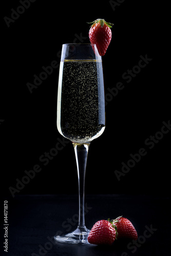 Obraz na płótnie champagne sparkling white wine glass and bottle on black background with strawberry garnish gold ribbon w salonie
