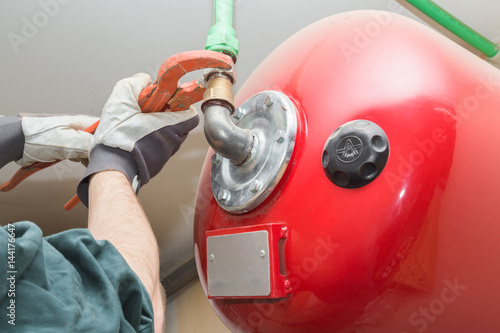 Man's hand in protective glove working with an adjustable wrench at water heater boiler equipment. Plumbing.