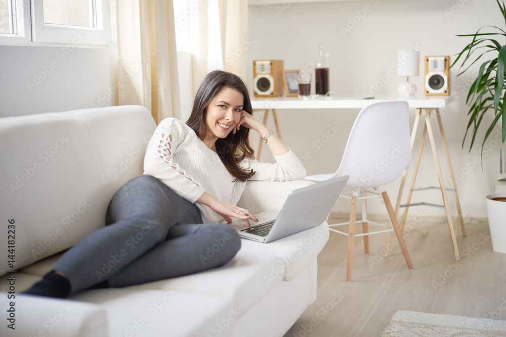Smiling businesswoman laying on sofa and using laptop computer for communication, chatting Smiling businesswoman laying on sofa and using laptop computer for communication, chatting