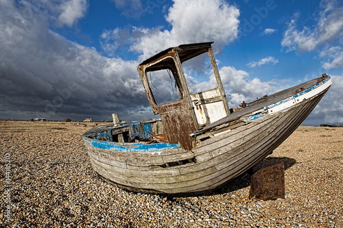 An abandoned wooden fishing boat  with wheelhouse  on the beach under blue sky and darkening clouds