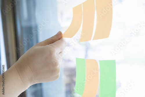 Close up shot of hands of woman sticking adhesive notes on glass wall in office