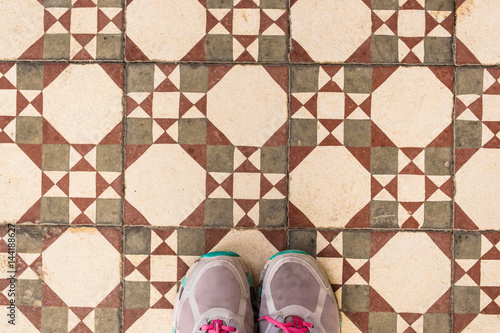 Selfie of feet with sneaker shoes on art pattern tiles floor, top view photo