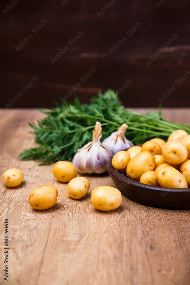Potatoes in plate. Carrot tops, garlic and raw new potato. Fresh natural vegetables. Organic bio food on rustic wooden table. Potatoes in plate. Carrot tops, garlic and raw new potato. Fresh natural vegetables. Organic bio food on rustic wooden table.