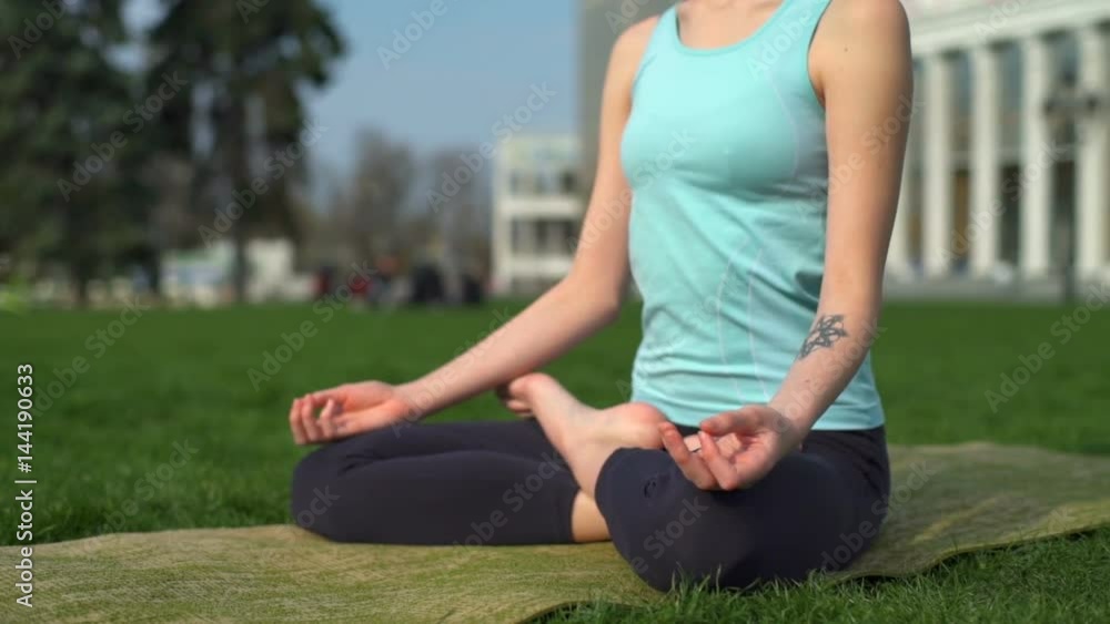 Young slim female siting on mat in lotus pose and meditate close up slow motion Young slim female siting on mat in lotus pose and meditate close up slow motion