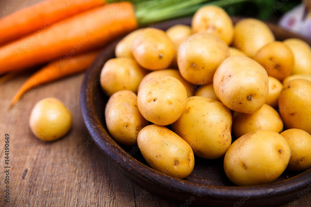Potatoes in plate. Carrot, garlic and raw new potato. Fresh natural vegetables. Organic bio food on rustic wooden table. Potatoes in plate. Carrot, garlic and raw new potato. Fresh natural vegetables. Organic bio food on rustic wooden table.