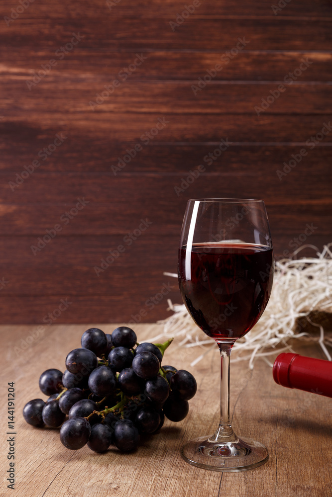 Red wine. Bottle and Wineglass with dark grapes branch. On rustic wooden background.