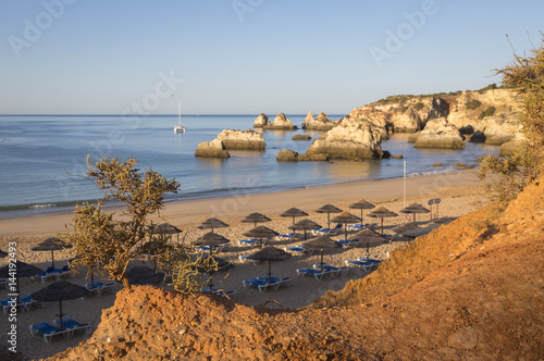 The newly risen sun shines on cliffs and bathhouse of Praia do Alemao Portimao Algarve Faro District Portugal Europe photo