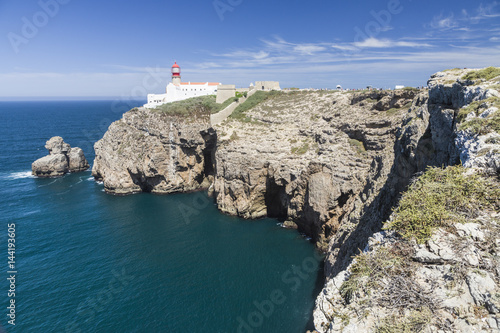 The cliffs and lighthouse overlooks the blue Atlantic ocean at Cabo De San Vicente Sagres Algarve Portugal Europe photo
