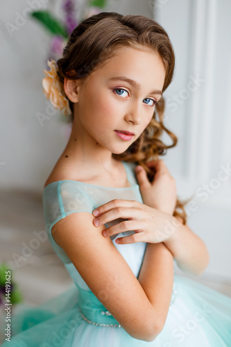 portrait of a beautiful young girl with blue eyes, make up and hairstyle in a lush turquoise dress in a studio with flower decoration