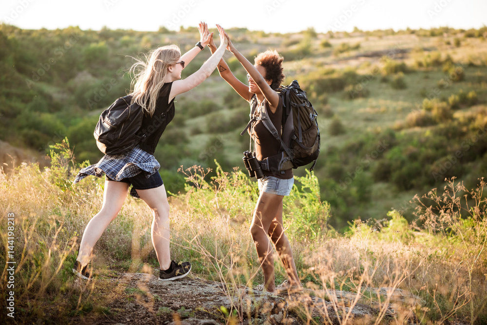 Girls with backpacks smiling, giving highfive, traveling in canyon.