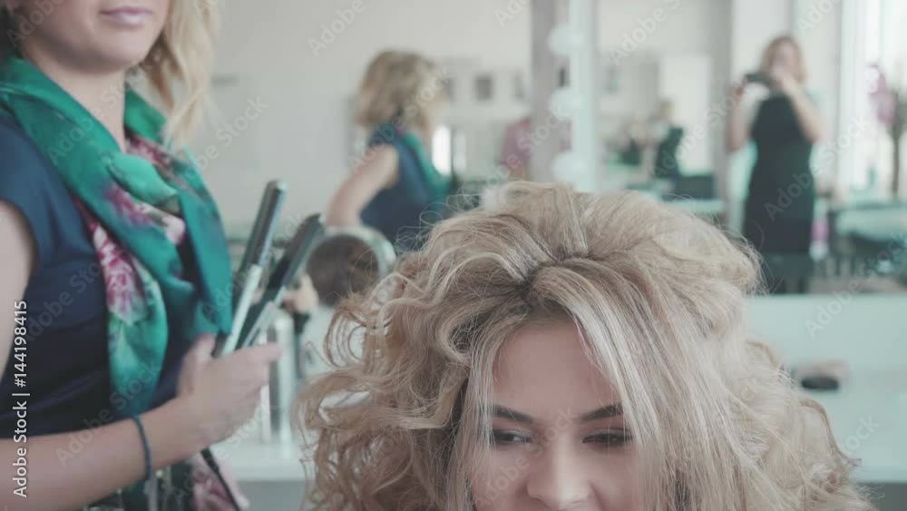 Portrait of a young woman in a beauty salon: creating a magnificent setting from curls. A blonde in a hairdresser does a beautiful hairstyle. Hair care and creating an image.