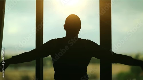 Man opens the curtains in the morning raises his hands and stretch oneself. Young man opens big window curtains and lets the sun light in the room