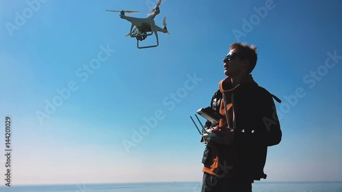 Quadrocopter drone takes off from the pilot's hand and hovers over the guy. The guy starts a drone on a green glade against the backdrop of the sea and cargo ships. Slow motion (120 fps).