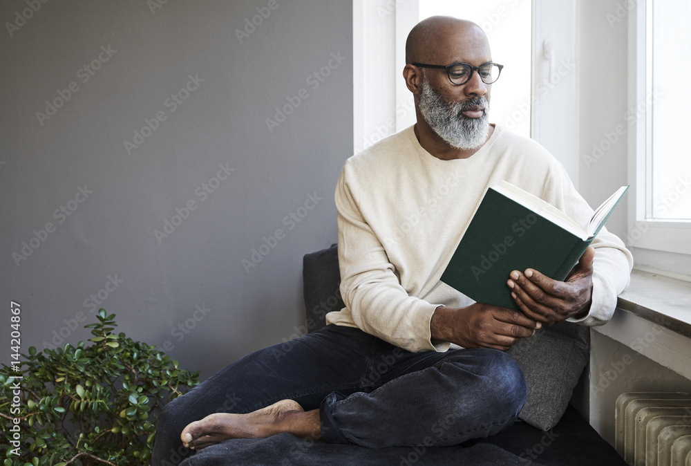 Mature man sitting at window, reading a book Mature man sitting at window, reading a book