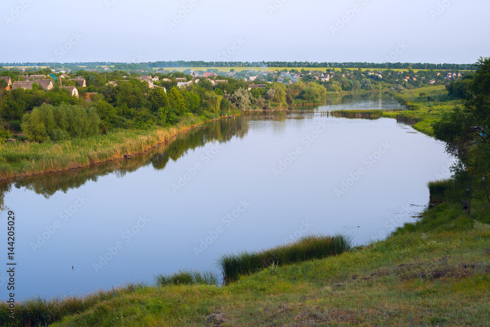 Calm river flows through a village in the midst of a green prairie Calm river flows through a village in the midst of a green prairie