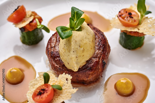 Beef filet dinner entree with garnish and brown sauce displayed on a white dinner plate. Horizontal shot.