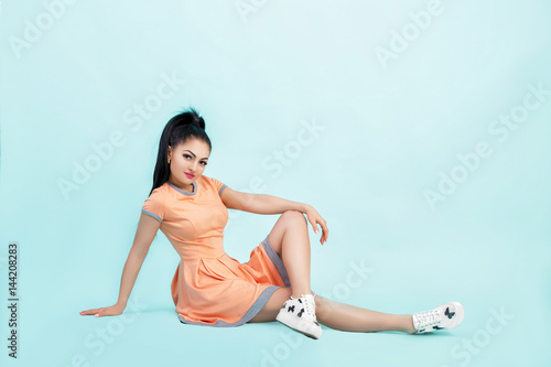 smilling young brunette woman in orange dress sitting on floor on blue background. 