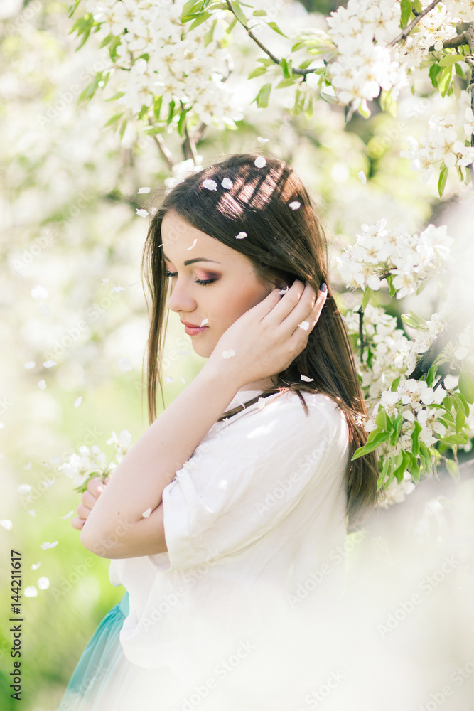 Outdoor Portrait of a Beautiful Brunette Woman in Color dress among Blossom Cherry Trees