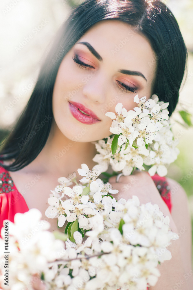 Outdoor Portrait of a Beautiful Brunette Woman in Color dress among Blossom Cherry Trees