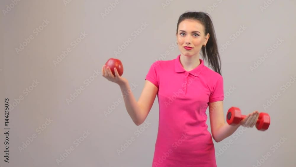 Elements of a healthy lifestyle. Attractive young woman chooses apple and dumbbells Elements of a healthy lifestyle. Attractive young woman chooses apple and dumbbells