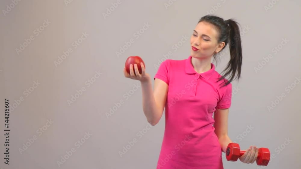 Attractive young woman chooses apple and dumbbells. Elements of a healthy lifestyle. Attractive young woman chooses apple and dumbbells. Elements of a healthy lifestyle.