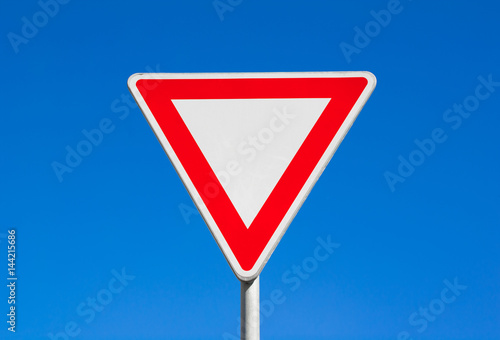 Give way / Yield - red and white triangle. Clear blue sky is behind road sign.