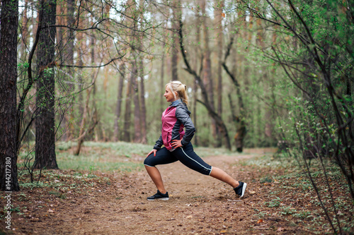 young beautiful girl doing workout in the woods. Blonde girl tracksuit doing exercises