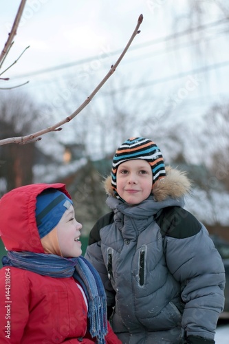 Two boys in colorful clothes  playing outdoors during the winter. Active winter vacation with children on cold days. Happy friends with a fun slide down the hill on the street in the village. Evening.