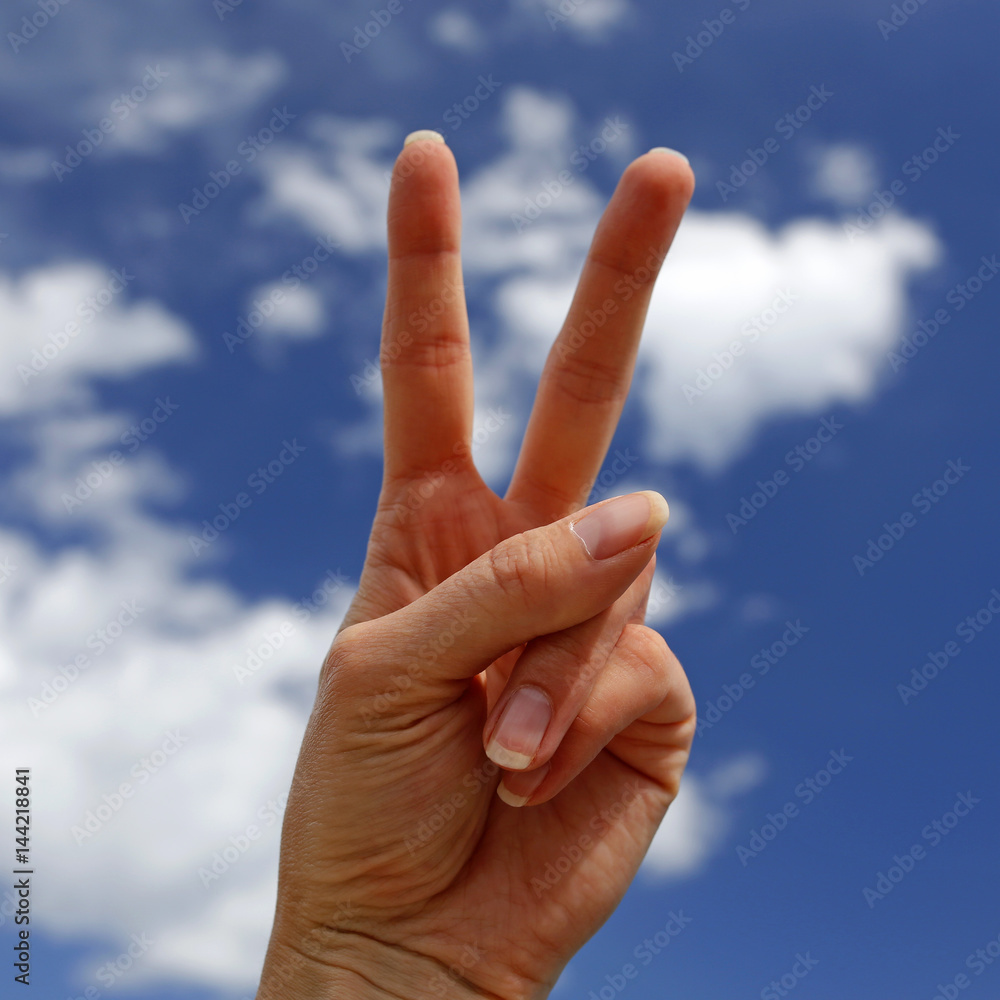 hand showing victory sign with blue sky in the background hand showing victory sign with blue sky in the background