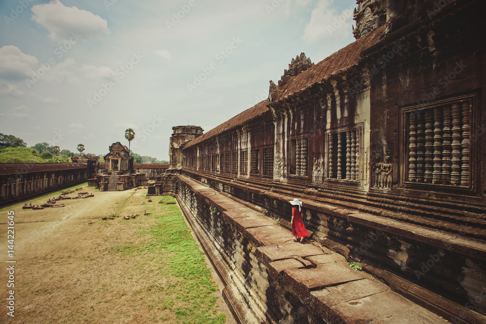 Fototapeta premium Girl in red dress walking through Angkor Wat temple, Siem Reap, Cambodia