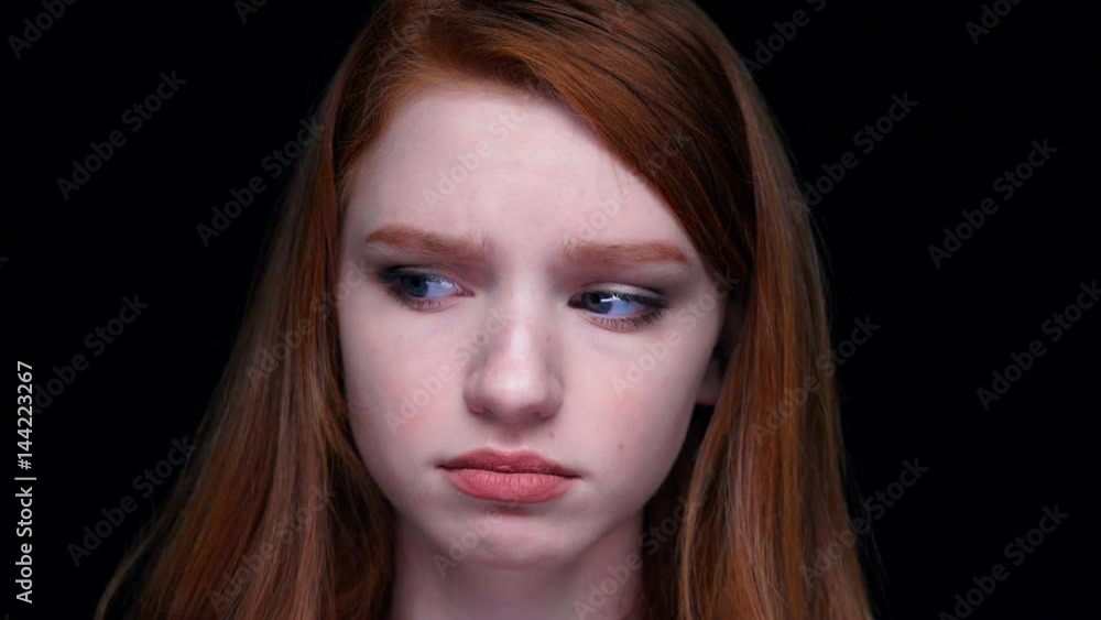 Close-up of unhappy dissatisfied young red haired woman looking at camera isolated over black Close-up of unhappy dissatisfied young red haired woman looking at camera isolated over black