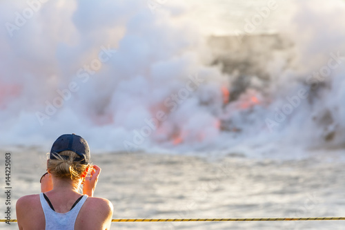 Fototapeta Naklejka Na Ścianę i Meble -  Tourist photographing the lava pouring into the sea in Volcanoes National Park, Big Island, Hawaii