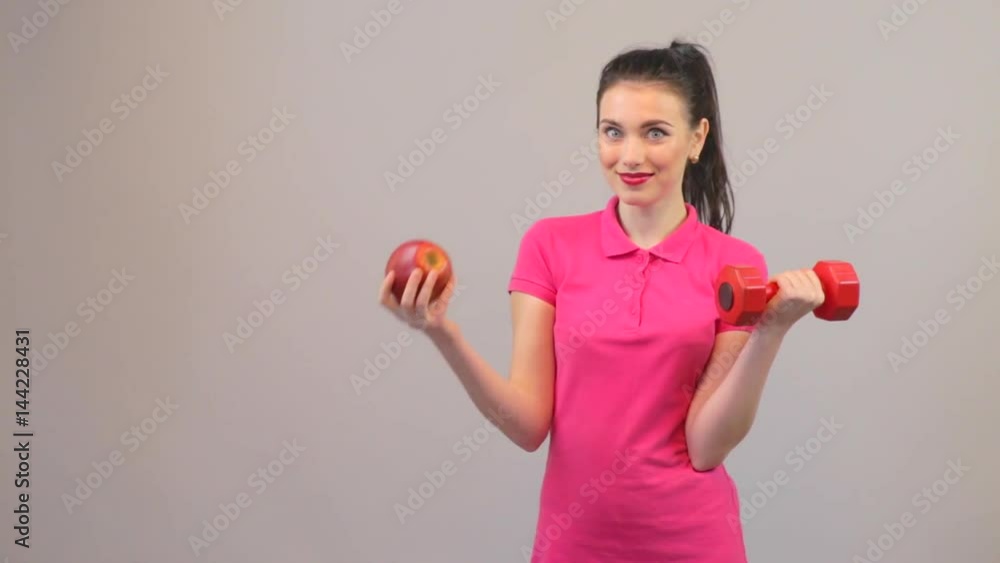 Attractive young woman chooses apple and dumbbells. Elements of a healthy lifestyle. Attractive young woman chooses apple and dumbbells. Elements of a healthy lifestyle.