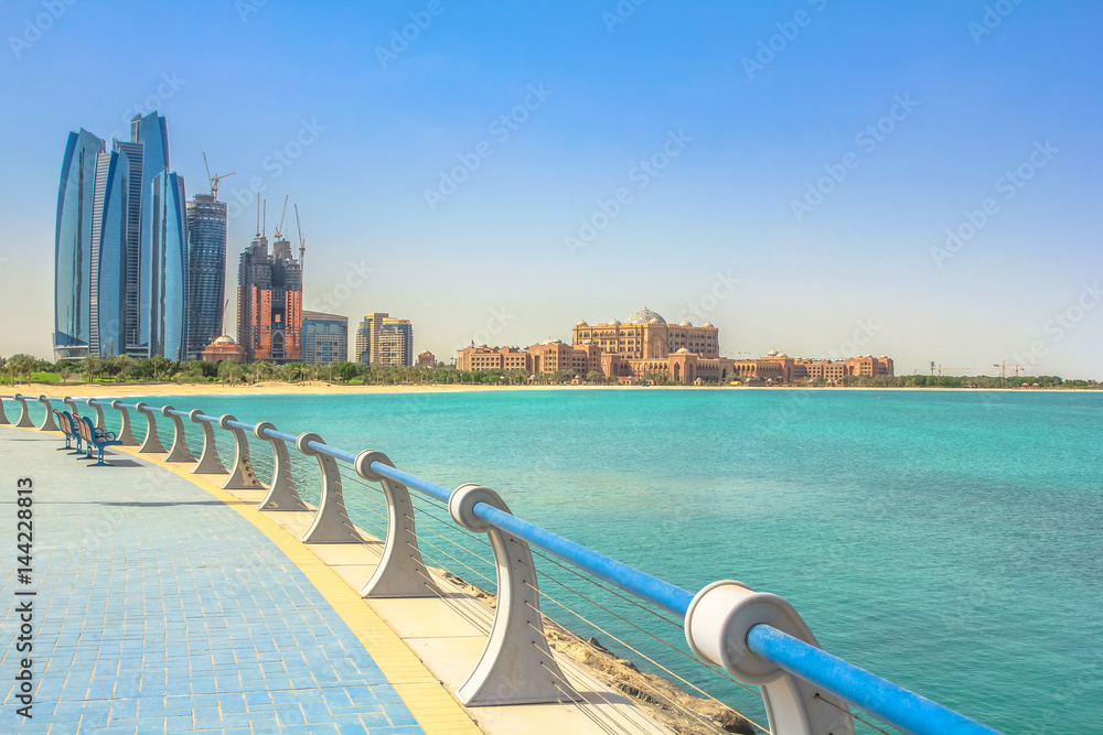 Dhabi skyline in the blue sky from Corniche in Abu Dhabi, United Arab Emirates, Middle East. Modern skyscrapers and landmark on background. Summer holidays concept. Sunny day, travel vacations.