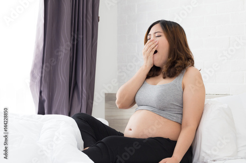 Sleepy asian pregnant woman yawning in bed at home