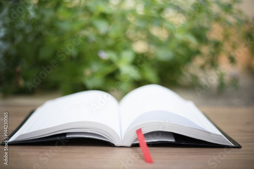An open book on  wooden table at home garden with nature bokeh background
