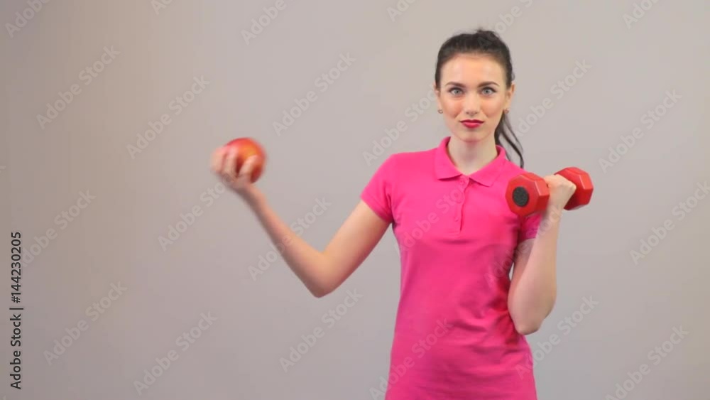 Elements of a healthy lifestyle. Attractive young woman chooses apple and dumbbells Elements of a healthy lifestyle. Attractive young woman chooses apple and dumbbells