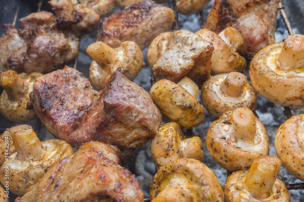 Pieces of tasty pork meat cooking with field mushrooms outdoor on smouldering carbons