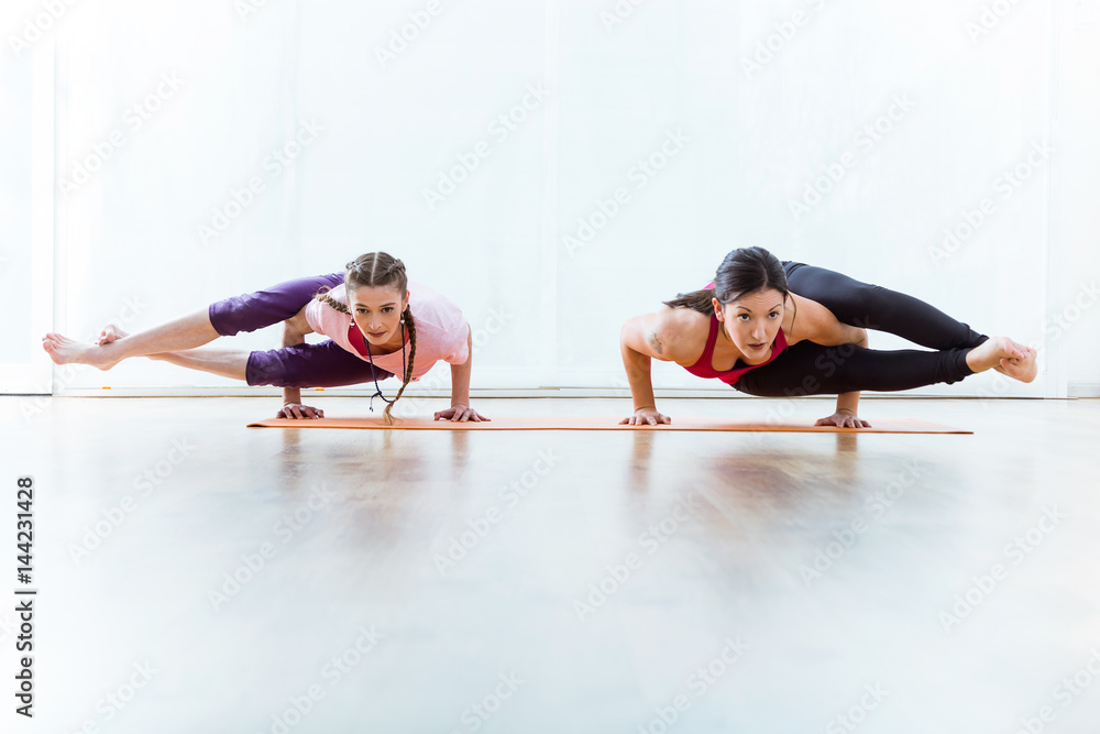 Two beautiful young women practicing yoga at home.